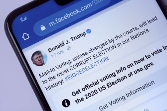 A close-up of a smartphone screen displaying a Facebook post by Donald J. Trump discussing concerns about mail-in voting and election integrity.