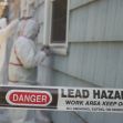 Workers in protective gear addressing a lead hazard at a residential property, with a warning sign indicating the area is restricted. Workers in protective gear addressing a lead hazard at a residential property, with a warning sign indicating the area is restricted.