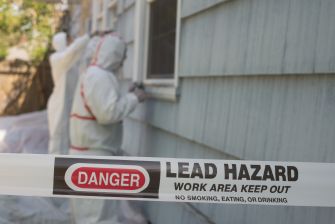Workers in protective gear addressing a lead hazard at a residential property, with a warning sign indicating the area is restricted.
