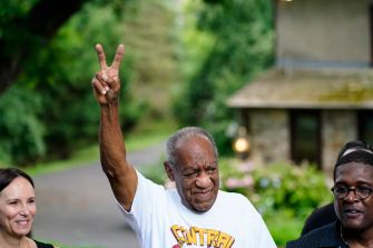 Bill Cosby raising his hand in a victory gesture while surrounded by supporters after his release from prison.