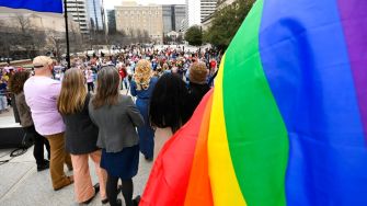 A crowd gathered at a rally with a prominent rainbow flag displayed in the foreground, advocating for drag shows and LGBTQ+ rights in Tennessee.