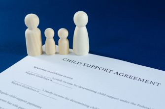 Wooden figurines representing a family stand beside a child support agreement document.