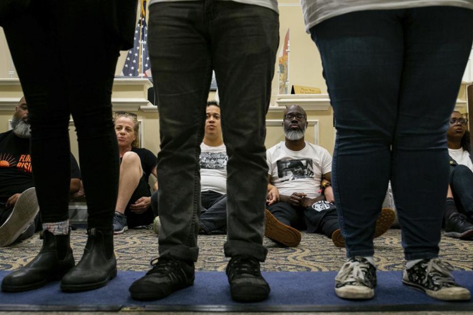 Dozens of activists stage a sit-in outside Florida Gov. Ron DeSantis' office and force people to step over them to reach DeSantis' office as they speak out against the governor and his policies. (Alicia Devine/Tallahassee Democrat via AP)