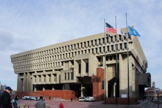 Boston City Hall with three flagpoles displaying the U.S. flag, Massachusetts state flag, and a third empty flagpole.