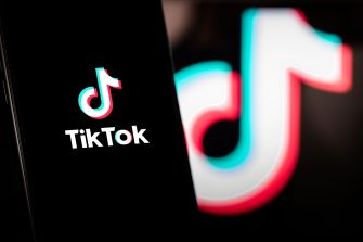 Close-up of a smartphone displaying the TikTok logo and a background image of the TikTok emblem illuminated in neon colors.