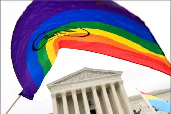 A close-up of a rainbow flag waving in front of the U.S. Supreme Court building, symbolizing LGBTQ rights and advocacy.