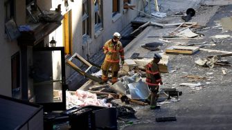 Two firefighters inspecting debris outside the Sandman Hotel after an explosion.