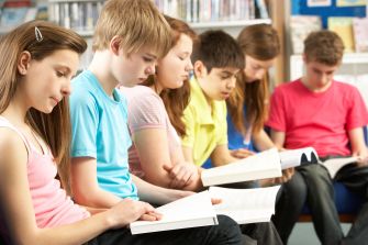 A group of children sitting in a row, focused on reading books in a library setting.