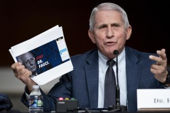 A man in a suit holding a printed sign with the text "FIRE DR. FAUCI" during a congressional hearing.