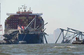 A cargo ship damaging a bridge after a collision in Baltimore, with emergency responders at the scene.