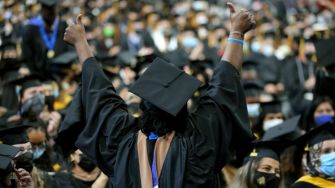 A jubilant graduate celebrating at a commencement ceremony, surrounded by the cheering crowd.