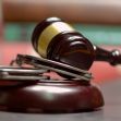 A wooden gavel resting on a sound block, with handcuffs beside it. A wooden gavel resting on a sound block, with handcuffs beside it.