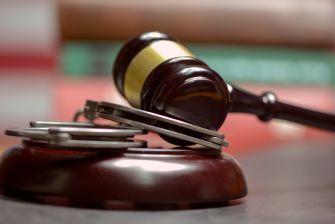 A wooden gavel resting on a sound block, with handcuffs beside it.