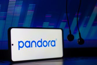 A smartphone displaying the Pandora logo with headphones in the foreground, set against a colorful digital backdrop.