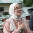 A woman wearing a hijab and glasses speaks passionately, expressing gratitude and emotion after her release from detention, with two men in formal attire standing beside her. A woman wearing a hijab and glasses speaks passionately, expressing gratitude and emotion after her release from detention, with two men in formal attire standing beside her.