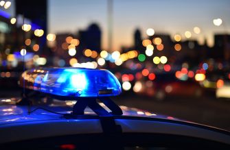 A police car with a flashing blue light at dusk, surrounded by blurred city lights and traffic.