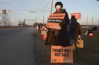 A protester holding signs against the death penalty outside a federal prison during the execution of Lisa Montgomery.