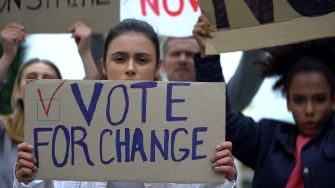 Protesters holding signs advocating for voting rights and reforms, with a focus on the message "VOTE FOR CHANGE".