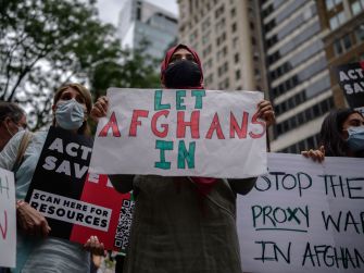 A group of protesters holding signs advocating for Afghan nationals to be allowed entry into the United States, emphasizing the urgency of the situation.