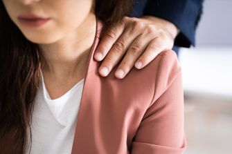 A close-up of a woman's shoulder with a man's hand placed on it, symbolizing inappropriate physical contact in a workplace setting.