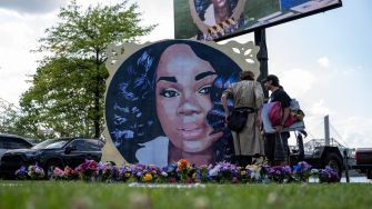 Memorial mural of Breonna Taylor with visitors paying their respects, surrounded by flowers.