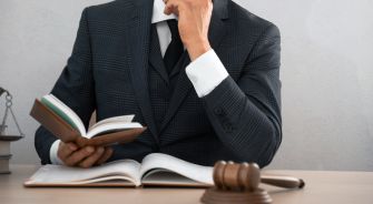 A lawyer in a suit reading a book at a desk with a gavel.