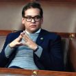 A man seated in a legislative chamber, dressed in a navy suit and glasses, looking contemplatively with hands clasped. A man seated in a legislative chamber, dressed in a navy suit and glasses, looking contemplatively with hands clasped.