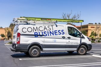 A Comcast Business service van parked in a lot, featuring the company logo and contact information.