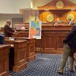 A man points to a map of Alabama's congressional districts during a legislative meeting, with officials seated at a table in the background. A man points to a map of Alabama's congressional districts during a legislative meeting, with officials seated at a table in the background.