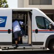 A USPS delivery worker loading mail into a postal van. A USPS delivery worker loading mail into a postal van.