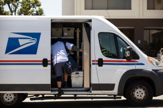 A USPS delivery worker loading mail into a postal van.