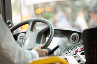 A close-up view of a bus driver's hands on the steering wheel inside a bus cockpit.