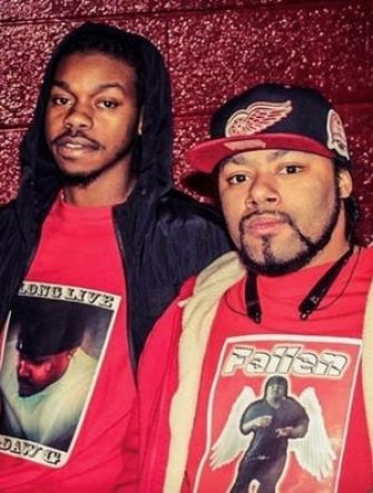 Two men posing together, both wearing red clothing and looking towards the camera.