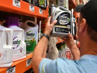A person examining a bottle of Roundup weed killer in a store aisle among other cleaning products.