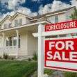 A house with a "Foreclosure" and "For Sale" sign in the front yard. A house with a "Foreclosure" and "For Sale" sign in the front yard.