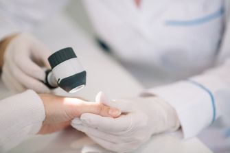 A dermatologist examining a patient's hand with a medical light.