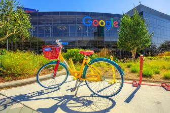 A colorful bicycle parked in front of the Google headquarters building, featuring the Google logo.