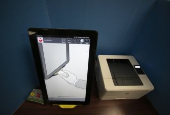 Voting machine and printer setup showing a touchscreen interface with instructional graphics.