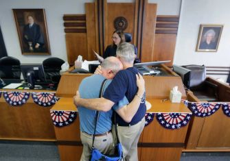 Two men embrace in a courthouse, symbolizing support and solidarity, against the backdrop of a legal setting.