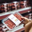 A person holding a package of ground beef in a grocery store aisle. A person holding a package of ground beef in a grocery store aisle.