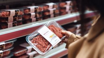 A person holding a package of ground beef in a grocery store aisle.