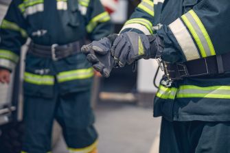 Firefighters adjusting their gloves while wearing protective gear, highlighting a lawsuit concerning toxic substances in firefighting equipment.