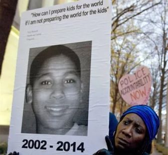 A person holding a sign with a photo of Tamir Rice and a quote about preparing children for the world, along with a smaller sign calling for police accountability.