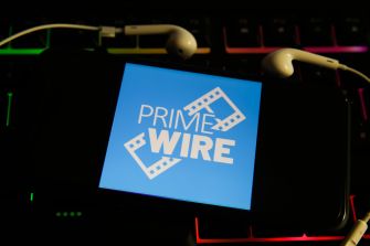 Logo of the streaming website PrimeWire displayed on a smartphone with earphones, set against a colorful keyboard backdrop.