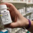 A hand holding a pill bottle of OxyContin, with shelves of other medication in the background. A hand holding a pill bottle of OxyContin, with shelves of other medication in the background.
