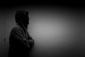 A silhouetted figure of a man in a hoodie leaning against a wall, conveying a sense of contemplation or vulnerability.
