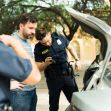 A police officer searching a vehicle while the driver looks on, amid a traffic stop. A police officer searching a vehicle while the driver looks on, amid a traffic stop.
