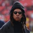 Jay-Z wearing sunglasses and a warm hat at a sporting event. Jay-Z wearing sunglasses and a warm hat at a sporting event.
