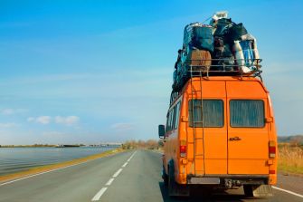 An orange bus on a road with luggage stacked on top, transporting migrants.