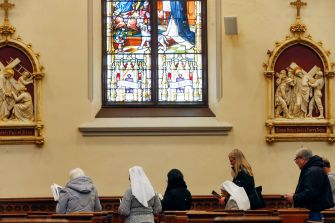 People praying in a church with stained glass windows and religious statues.